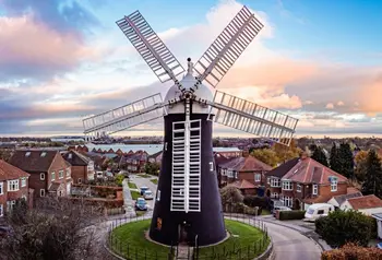 A windmill with houses in the background set against a blue sky