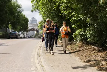 People with high visibility jackets, clipboards and binoculars walking within an urban nature spot in Newham, London