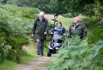 A man and woman walking alongside a woman in a mobility scooter on a path surrounded by plants at RSPB Minsmere