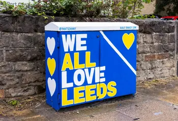A telephone cable cabinet decorated in blue and yellow, with the slogan 'We All Love Leeds'.