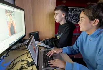 Two young adults sitting in front of multiple computer screens as they edit a video
