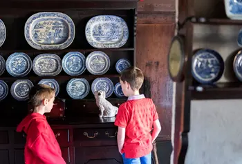 Two children, facing away, looking at a wall of traditional porcelain plates.