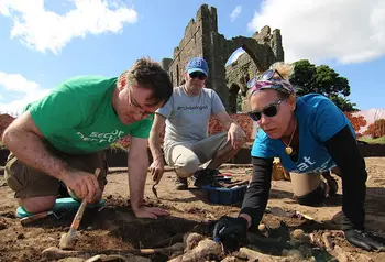 Three people use trowels and brushes to excavate around bones in an archeological dig