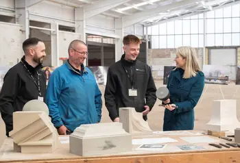 A group of stonemasons talk to Caroline Clark from the National Lottery Heritage Fund about their craft, discussing models of their work on a table in front of them.