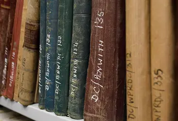A bookshelf of old books in an archive. The books have reference numbers written on their spines.