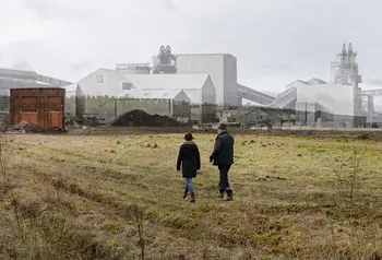 Two people walk across a field. In the background of the photo a historic photo of a colliery has been layered onto the photo