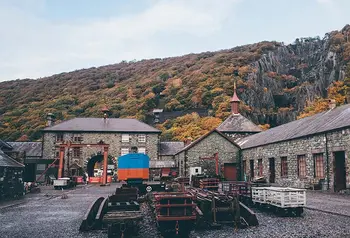 the courtyard of the National Slate Museum in Llanberis, north Wales, with stone factory buildings surrounding a courtyard with industrial equipment for processing slate, and the slate mine visible in the background