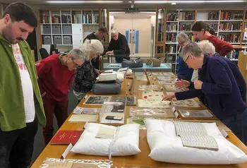 a group of people look at objects from a historical archive laid out on a long table
