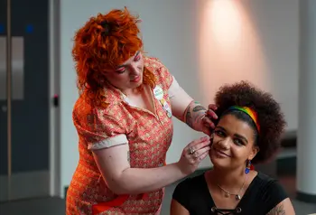 Two people preparing for a party. One person is having a temporary transfer applied to their face. 