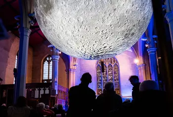 People look at a huge illuminated moon artwork suspended in a medium-size church