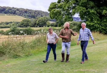 Three people are walking side by side in a pretty green landscape, they are talking and smiling