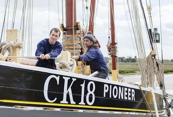 Two people pull a rope on the deck of a historic sailing vessel
