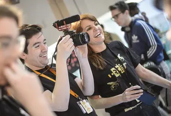 Two people wearing Reimagine, Remake, Replay tshirts using filming equipment at an event