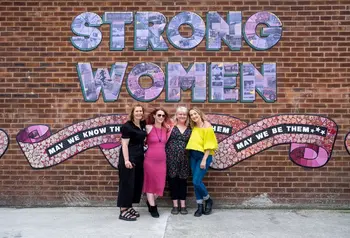 People standing in front of a ceramic mural that spells out the words Strong Women