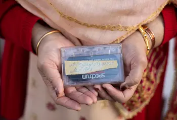 A woman's hands holding a cassette tape. She has bangles on her wrists and is wearing a red cardigan.