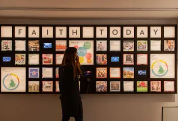 A visitor listens through an exhibition headset in front of a display of information about faith