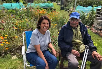 Two people smiling and sitting on camping chairs on an allotment