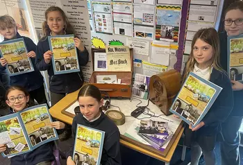 A group of school children hold books about life during the second world war and pose around a display related to the second world war 