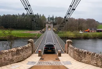 A car crosses the Union Chain Bridge, a small restored suspension bridge over a river.
