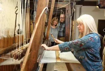 A person weaves cream coloured fabric on a wooden handloom
