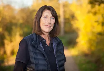 A woman stands in front of autumn trees