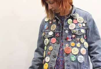 A young woman wearing a denim jacket covered in badges