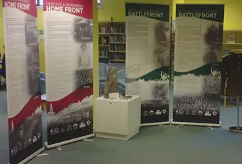A woman stands by four pull up displays, a model uniform on a mannequin and a glass case containing replica first world war objects