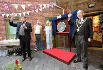 A group of people holding glasses gathered around an unveilled plaque