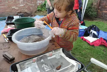 A child using a toothbrush to wash a sherd of pottery in a basin of water
