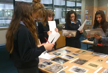 A group of young women standing around a table covered in old photographs