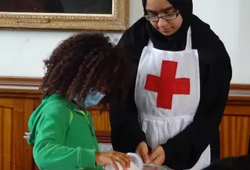 A young participant demonstrates wartime medical techniques to a young visitor
