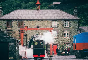 A small train billowing steam in the yard of the museum buildings