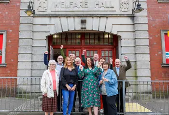 A group of different ages from the Tylorstown community celebrate outside the Welfare Hall, smiling and raising their hands in the air.