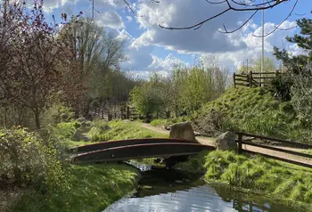 A pond with a bridge over it and footpath next to it on a sunny day
