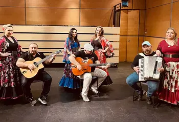 Three musicians with guitars and an accordion and four women dancers wearing traditional Eastern European dress.