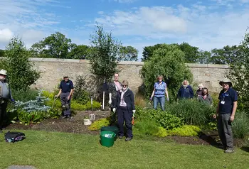 A group of gardening volunteers stand in a walled garden planting