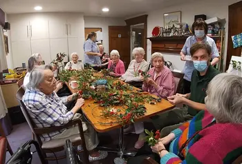 Group of people sitting around table making holly wreaths 