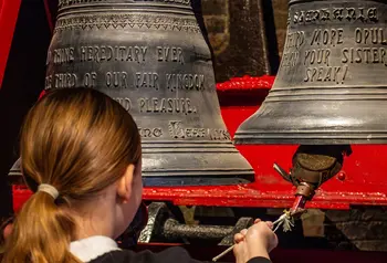 A visiting schoolgirl rings a cast iron bell on a bracket.