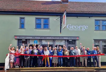 A crowd of people in front of The George pub stand behind a red ribbon