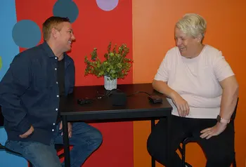Two people laughing with a recording device on the table in front of them