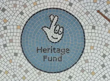 A mosaic constructed with tiles. In the middle of the mosaic is a teal circle, inside the circle is the text 'Heritage Fund' and The National Lottery's crossed fingers logo