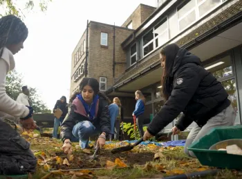 three young women dig a plot of ground marked with string with trowels