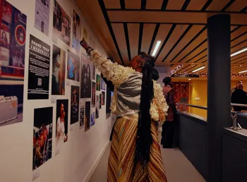 A person pointing at a gallery wall covered in pictures of dancehall artists