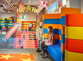 Young children are sat on colourful seating inside the museum, while others are stood on the stairs in the background