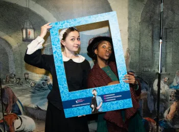 Image of two people in historic nursing outfits depicting Mary Seacole and Florence Nightingale, holding a frame to their faces