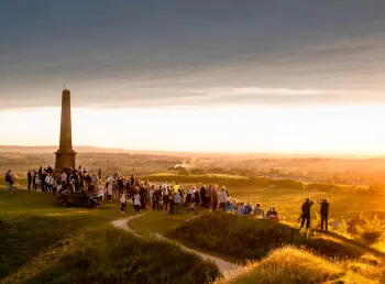 A large group of people stand on top of Ham Hill summit at sunset