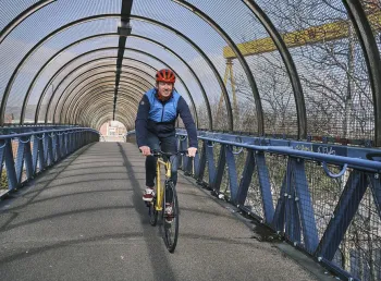 A man cycling on a bridge with the Harland and Wolff cranes visible in the background