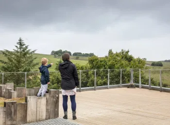An adult and child stand on decking, looking out over a countryside landscape