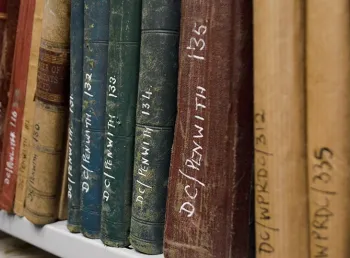 A bookshelf of old books in an archive. The books have reference numbers written on their spines.