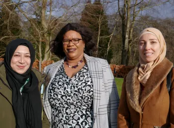 Three women from diverse ethnic communities are stood and smiling at the camera